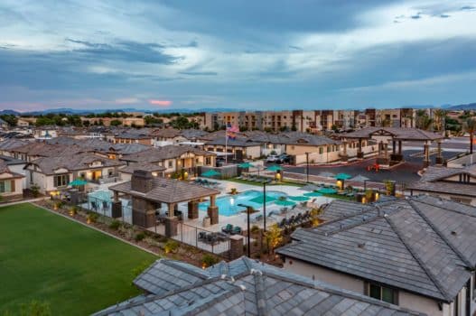 Aerial view of our rental homes in Peoria, AZ, featuring a pool area, grassy lawn, and a pink sunset.