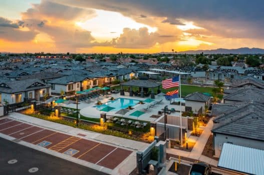 Aerial view of our rental homes in Peoria, AZ, featuring a pool area, Arizona flag, and a sunset over the mountains.