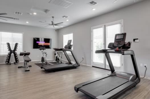 The fitness center at our rental homes in Peoria, AZ featuring wood grain floor paneling and treadmills.