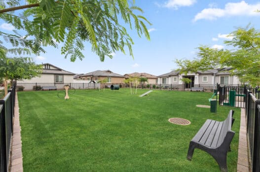 The dog park at our rental homes in Peoria, AZ, featuring a fenced in area with green grass, dog obstacles, and benches.